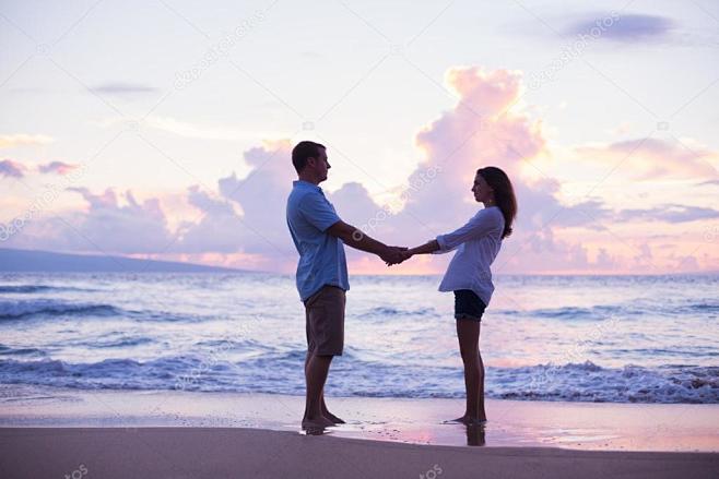 年轻的情侣们在日落时在热带度假海滩上散步