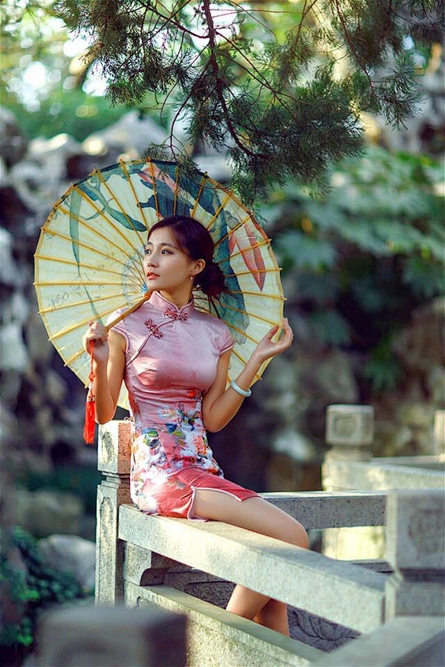 园林里撑着油纸伞的旗袍美女小麦色皮肤很健康